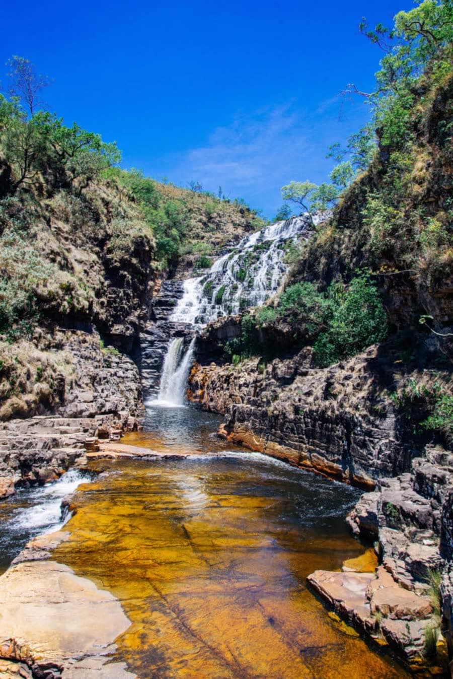 Salto em degraus sobre piscinas naturais douradas sob céu azul profundo